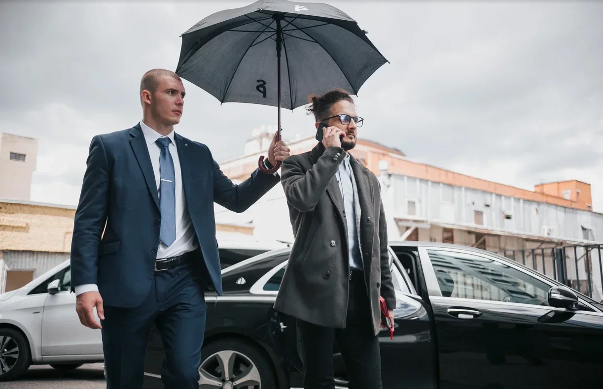 Two men beside a car under an umbrella